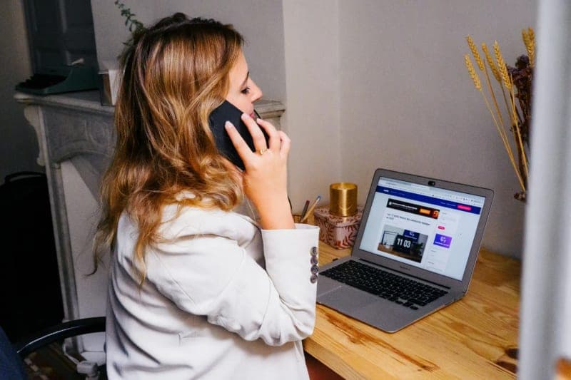 A cleaning business owner on a phone call at a desk, reviewing a bid follow-up tracker on a laptop screen (1)